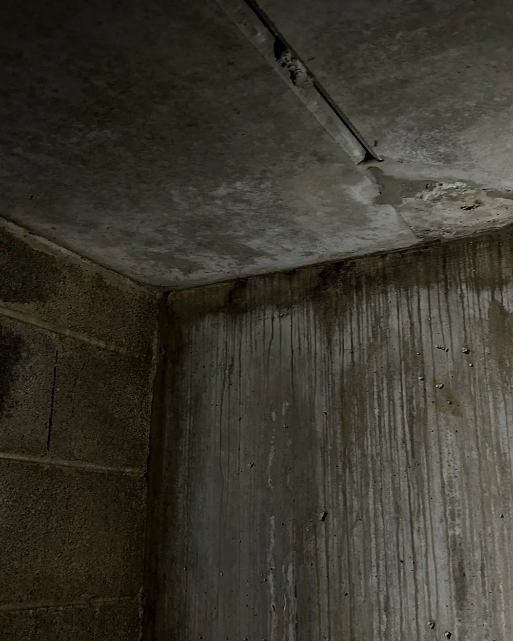 Coulures d'infiltration sur un mur et un plafond en béton, sous une toiture-terrasse